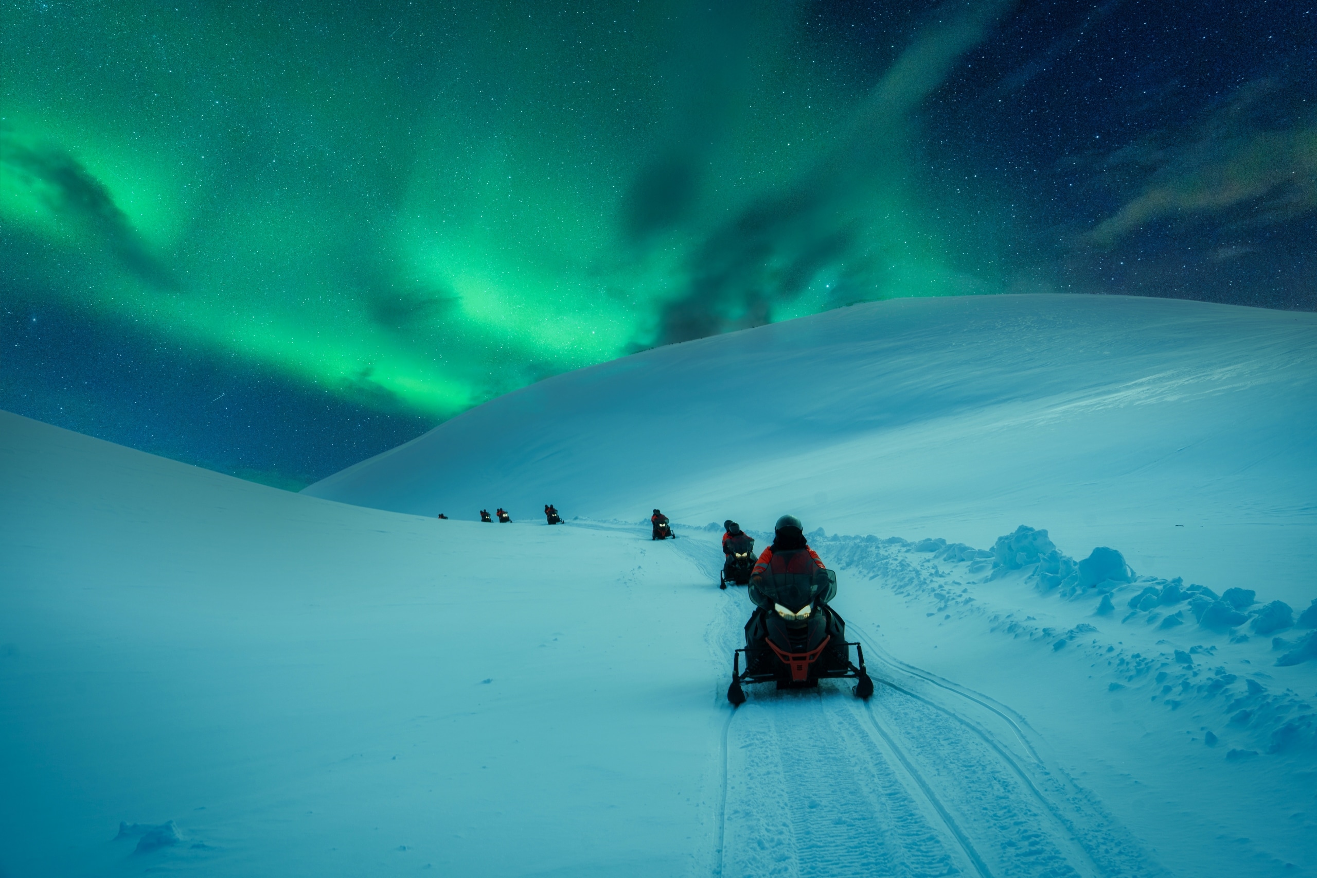 Snowmobiling tourists under Northern Lights during Polar Night in Svalbard